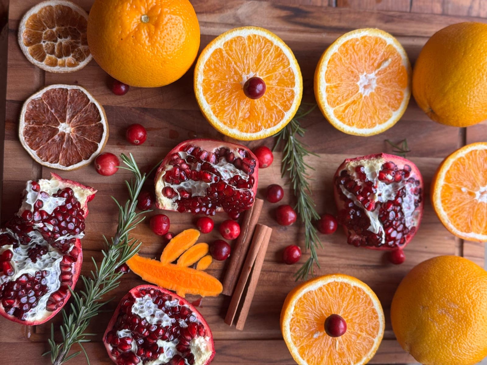 Halved oranges, pomegranates, cranberries, rosemary and cinnamon sticks on a wooden board