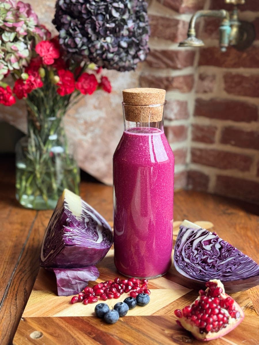 Purple juice in a corked glass bottle with red cabbage, pomegranate and blueberries